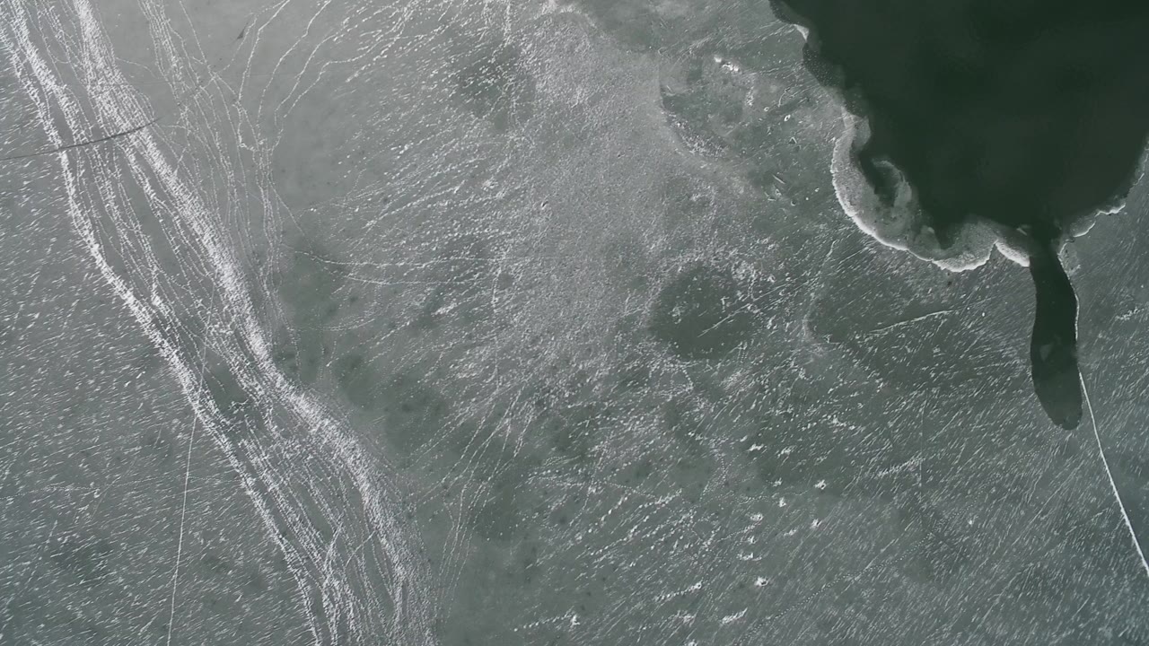 Overhead view of pale ice beside dark green water.