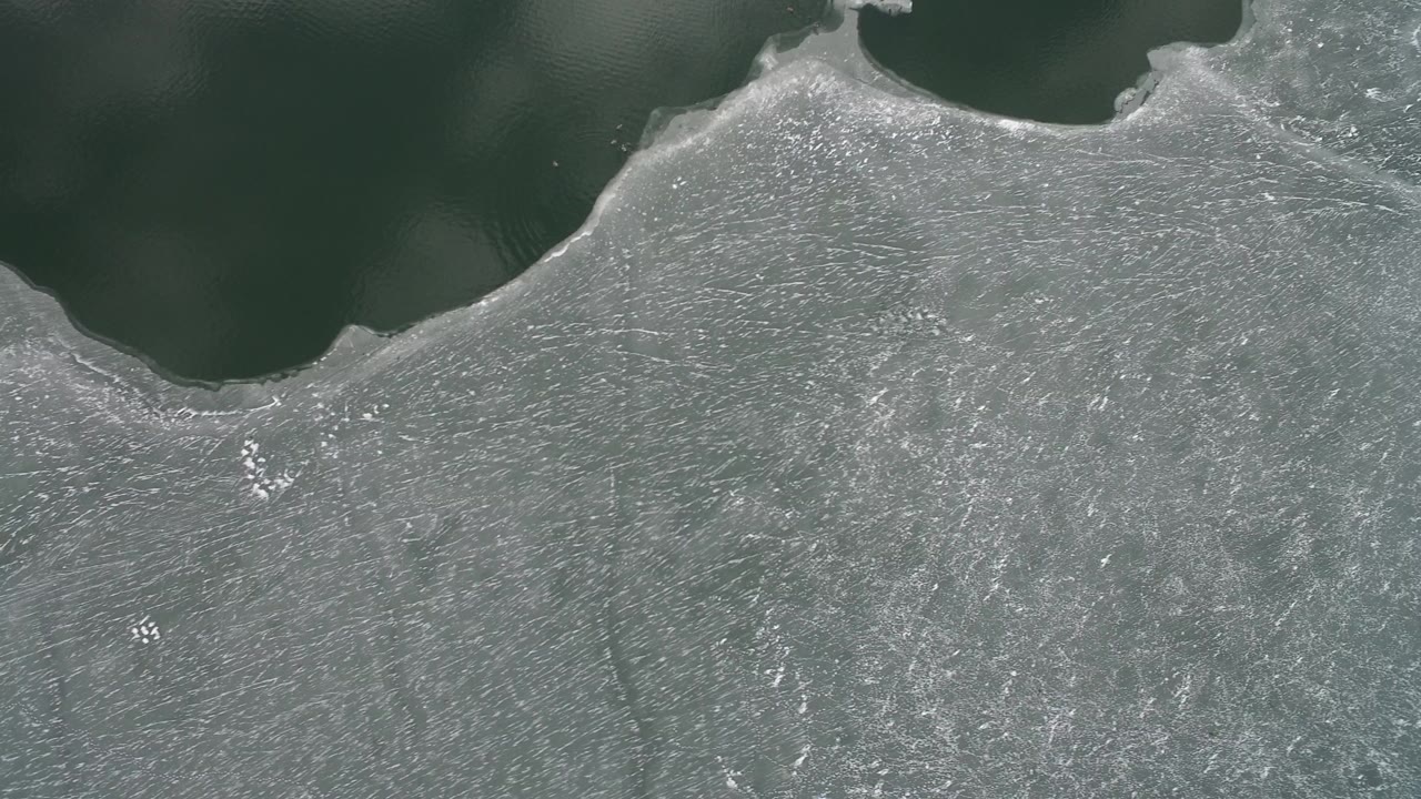 Overhead view of gray ice beside dark open water.