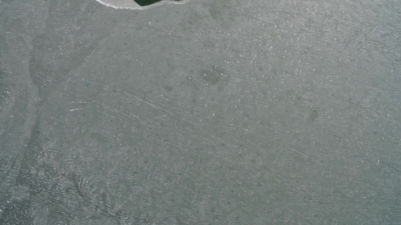 Overhead lake ice surface with faint scratches and dark water near the top.