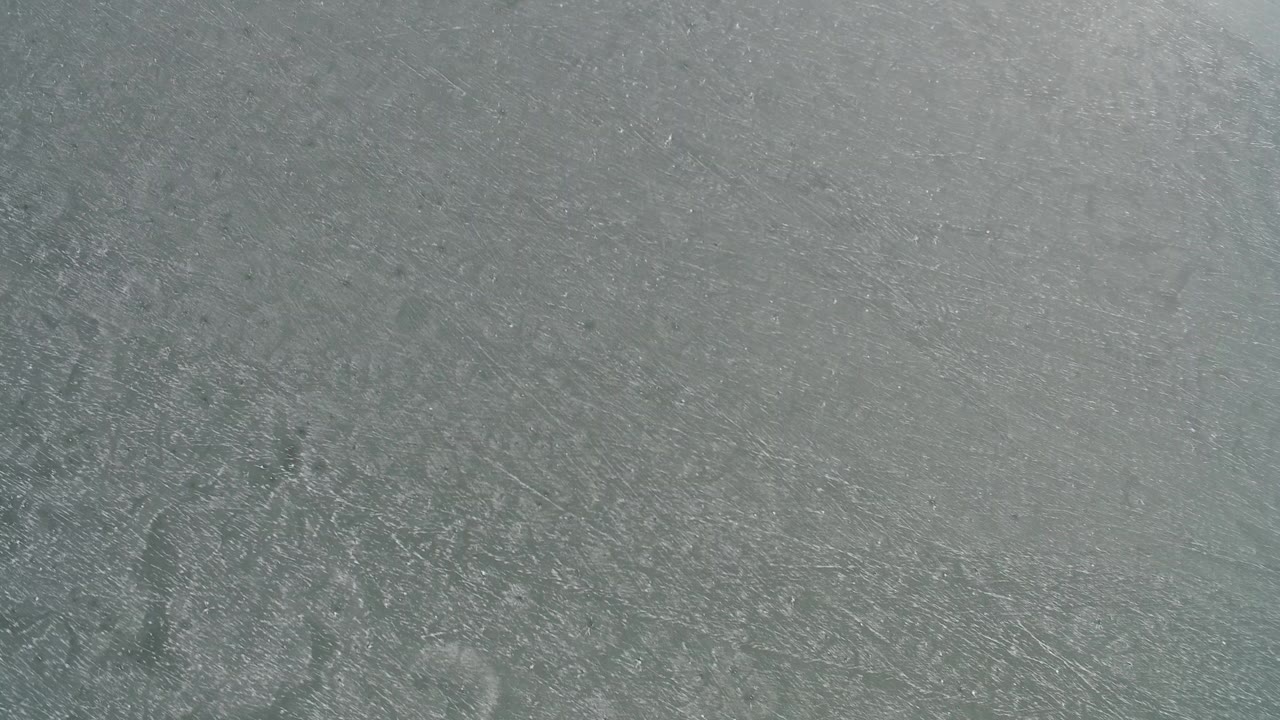 Overhead view of gray blue frozen water at Hidden Lake, Colorado, with dense scratch marks and no visible people.