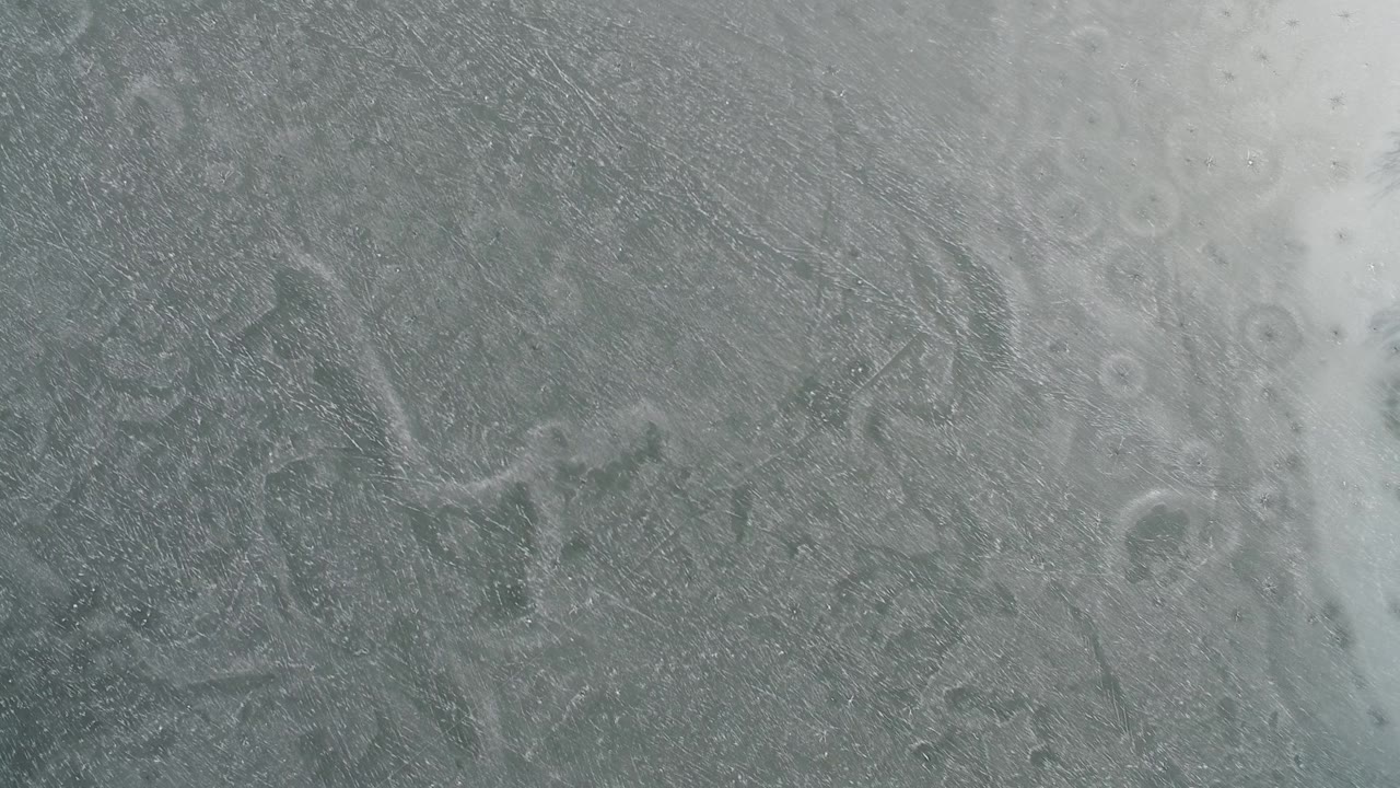 A pale diagonal band crosses the gray frozen surface at Hidden Lake, Colorado, with darker ice texture on both sides and no visible people.