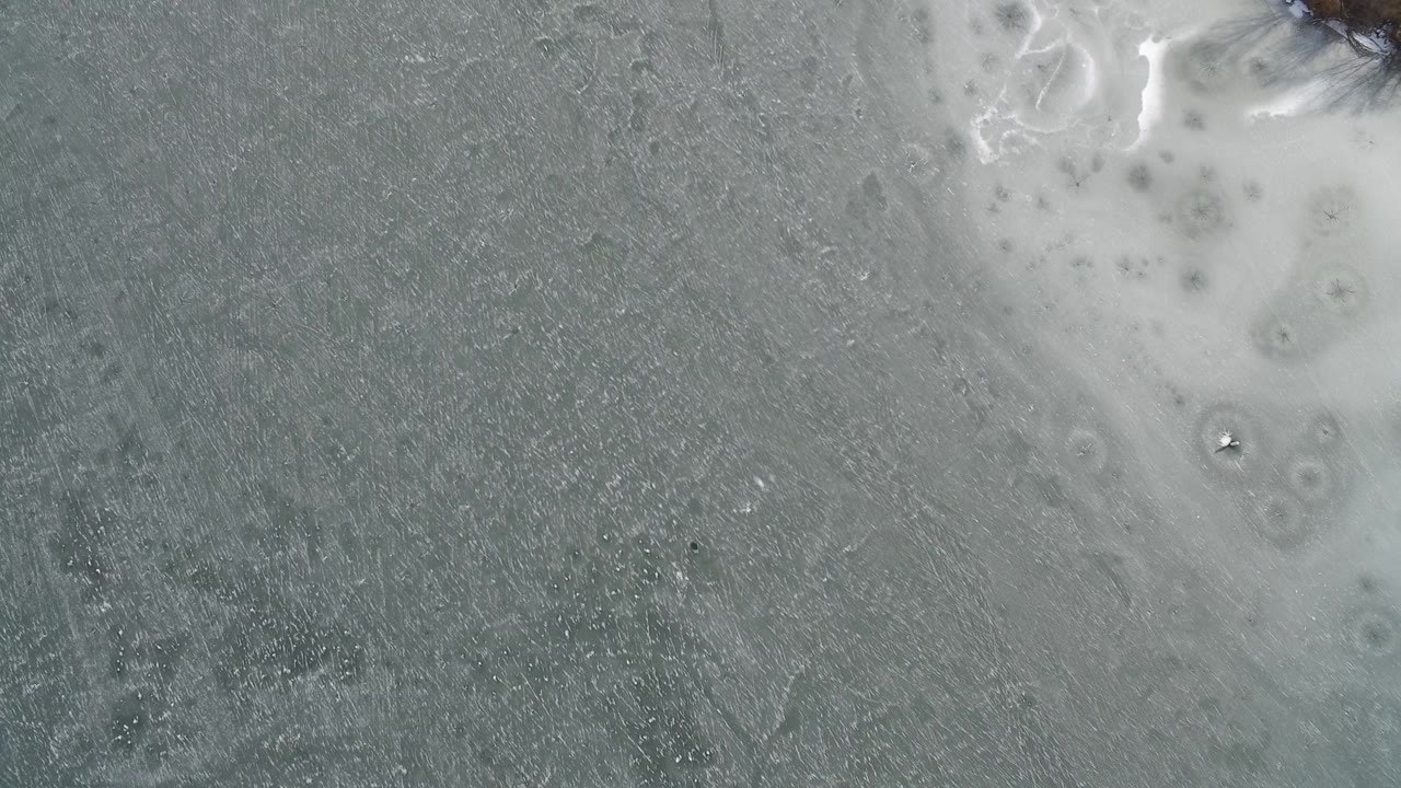 A close top-down frame from Hidden Lake, Colorado, shows mottled gray texture with clustered pale marks crossing the upper portion and no visible people.
