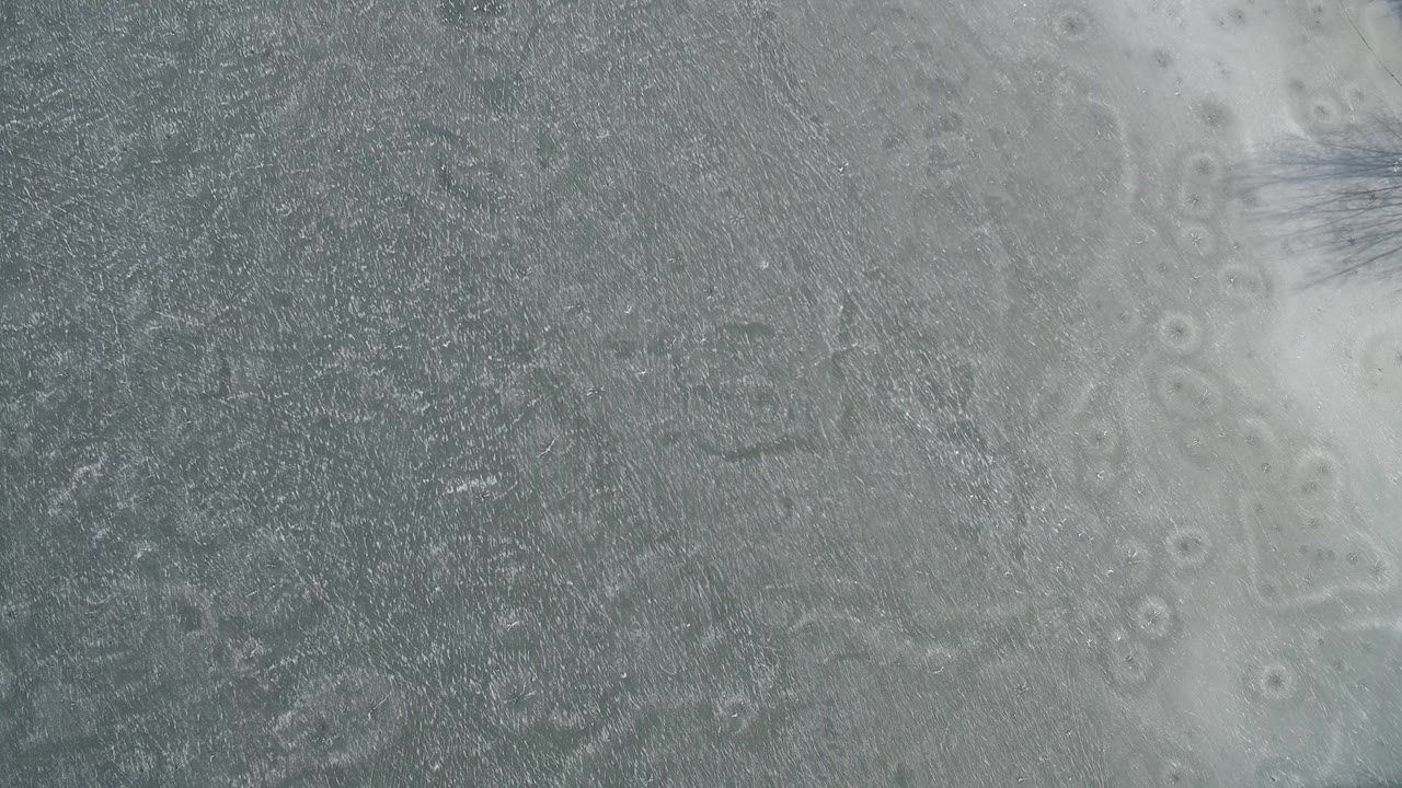 Frozen lake surface with pale ice bands and dark textured water areas.