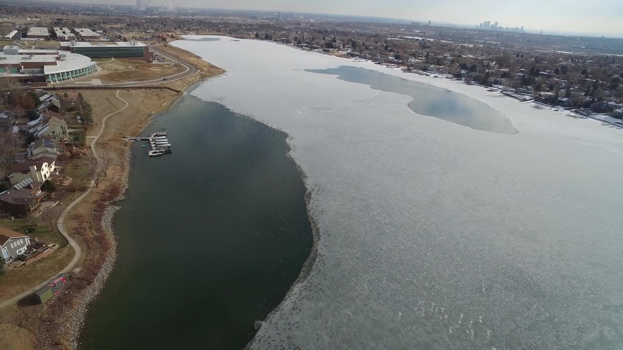 Aerial view of a partly frozen lake beside shoreline homes and docks.