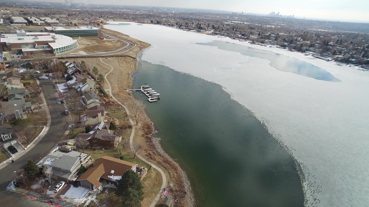 Aerial view of a partly frozen lake beside houses and curving roads.