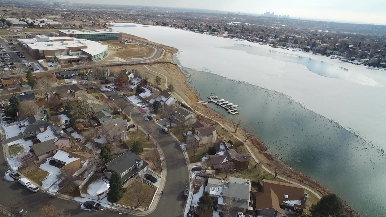 Aerial view of snowy homes beside an icy lake and docks.