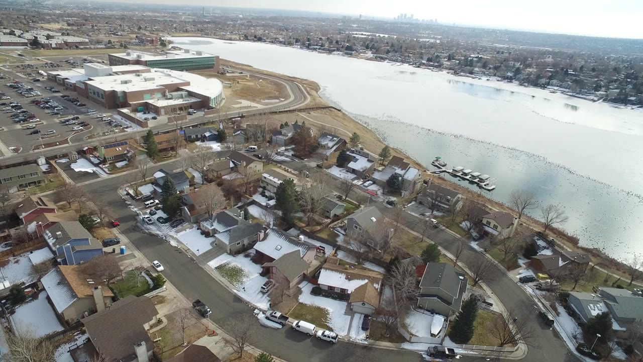 Early aerial frame over Hidden Lake, Colorado, showing snow-dusted private homes, curved streets, a large frozen lake, a parking area, and no visible people.