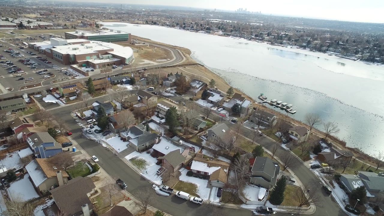 Aerial frame in Hidden Lake, Colorado, with rooftops and parked cars in the foreground, the frozen lake stretching across the middle, and no visible people.