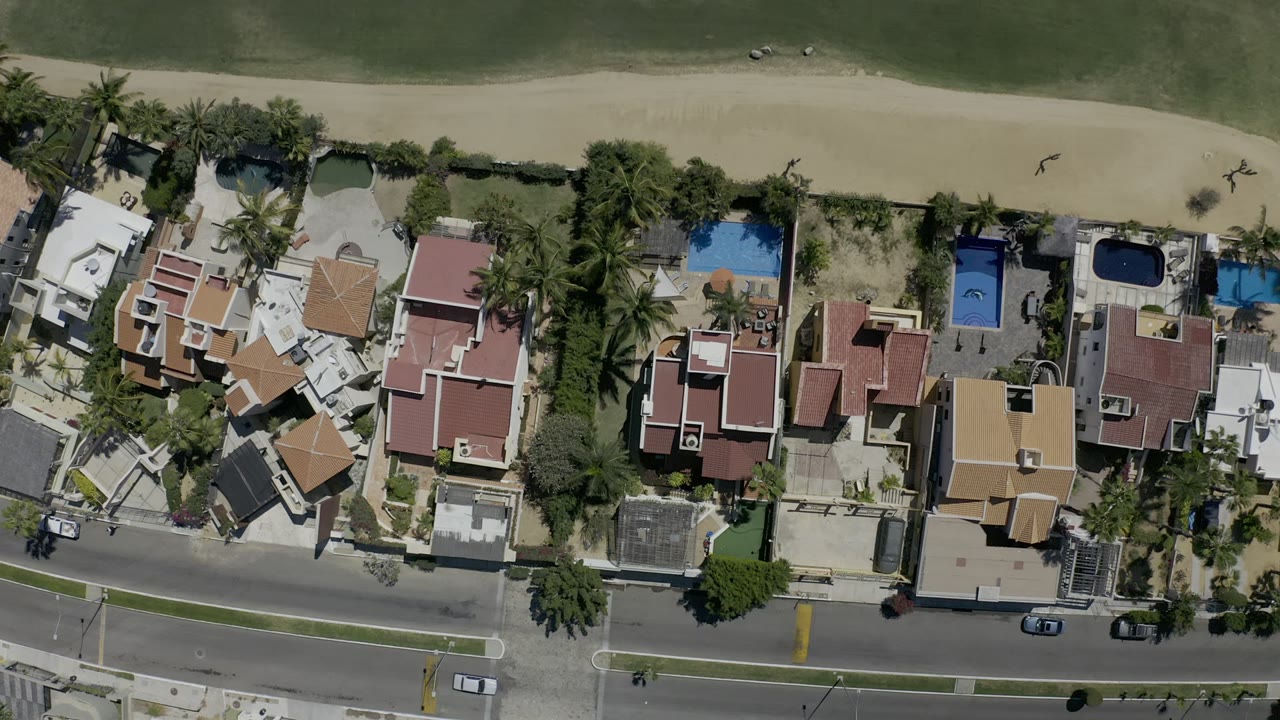 Overhead coastal homes beside a beach, road, and green water.