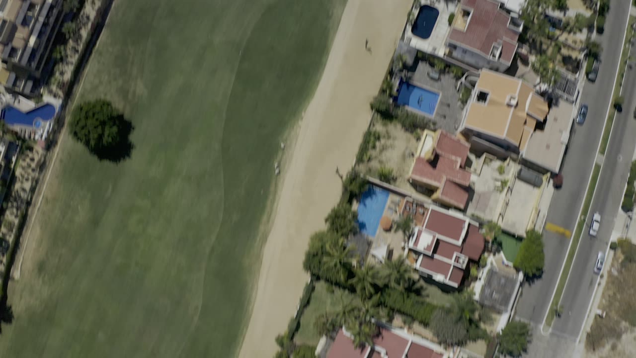 Top-down aerial view of golf fairway beside homes and a road.