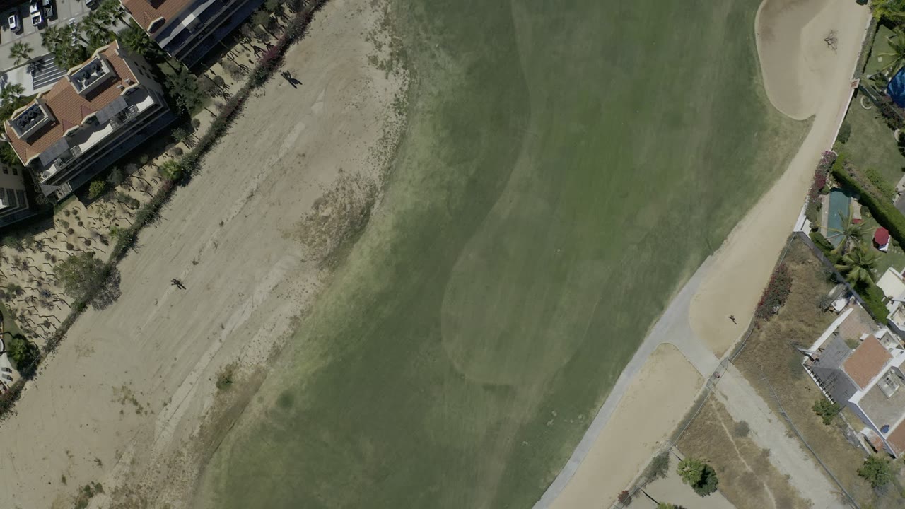 Overhead view of green fairway, sand, cart path, and homes.