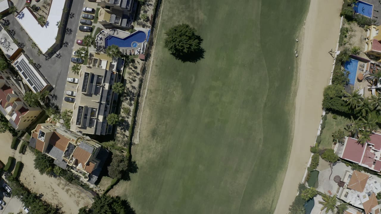 Top-down view of green grass beside homes, pools, roads, and sand paths.
