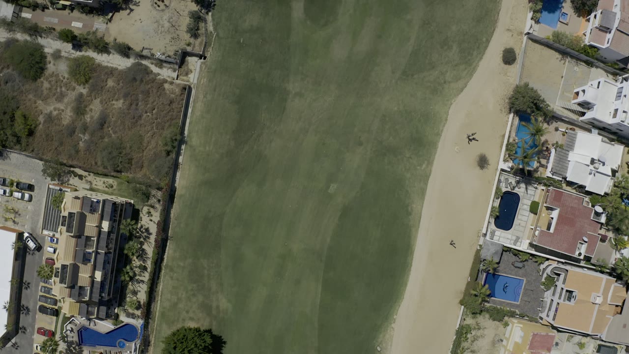 Overhead golf course fairway beside houses and pools.