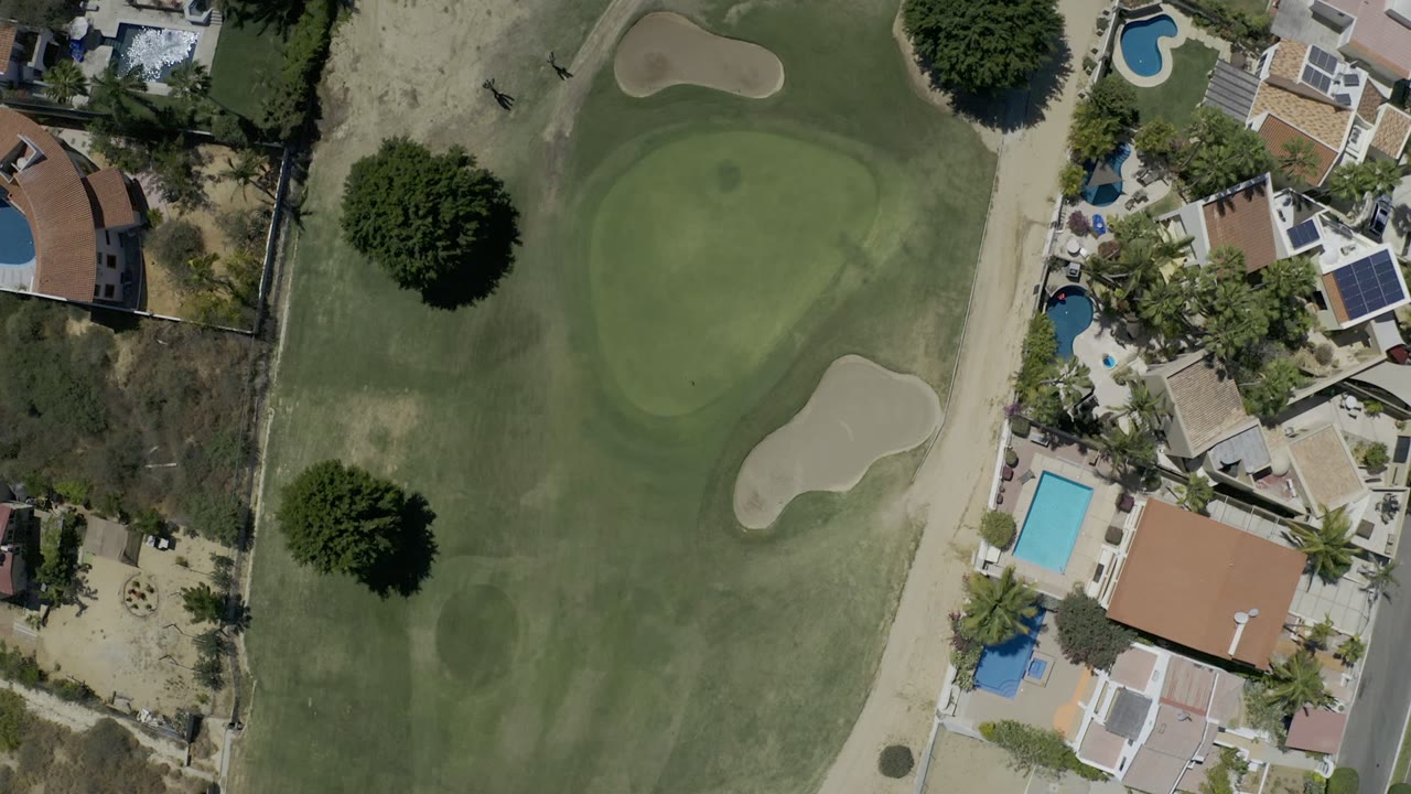 Overhead golf green beside homes and swimming pools.