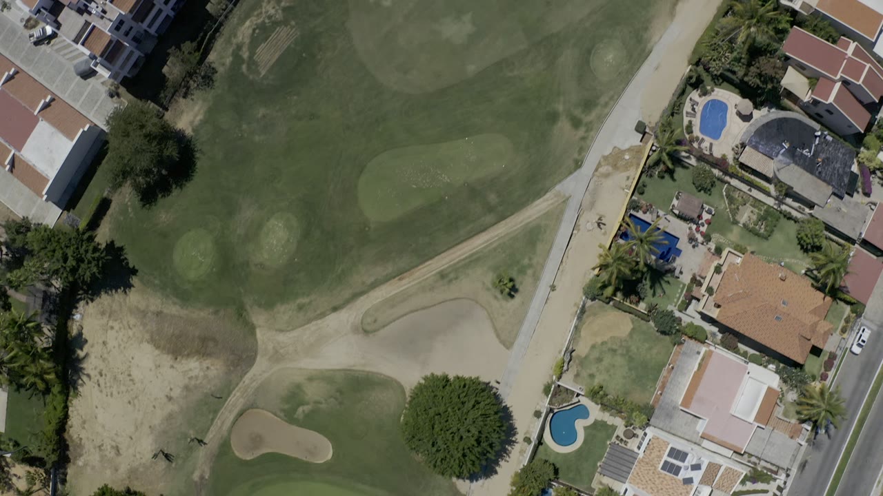 Overhead view of golf greens, road, homes, and swimming pools.