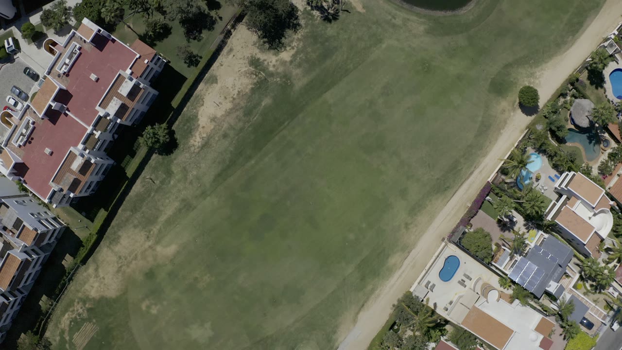 At 0:01, the Los Cabos overhead view centers more on the fairway and path, with residences and blue pools along the right edge and no visible people.