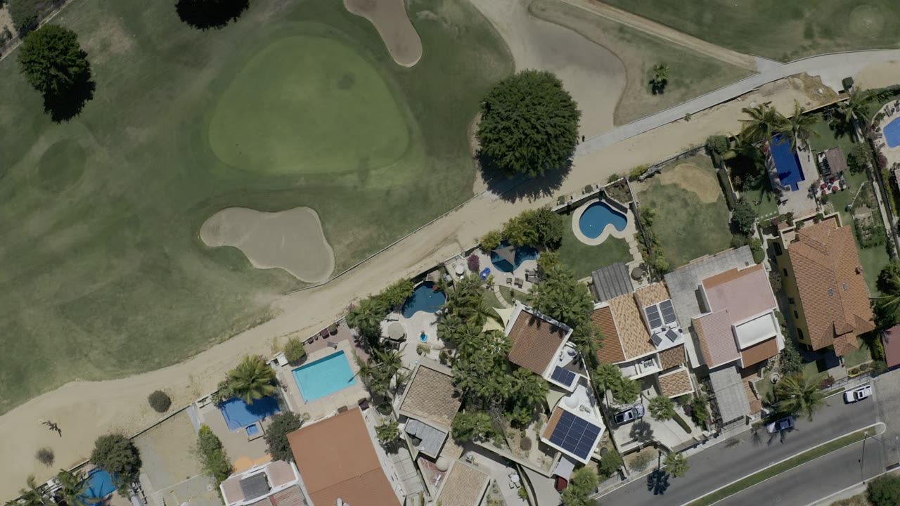 Overhead view of golf fairways, sand bunkers, homes, pools, and a road.
