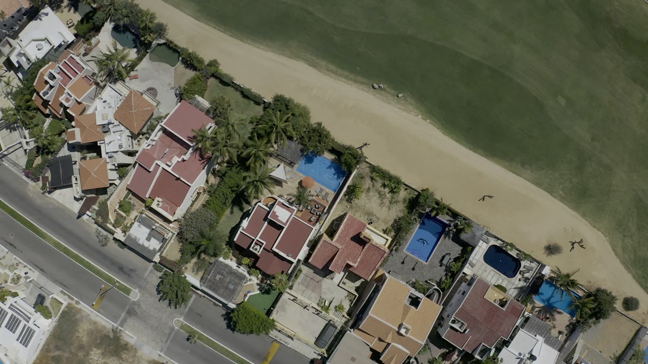 Overhead view of homes, pools, street, sand strip, and green turf.
