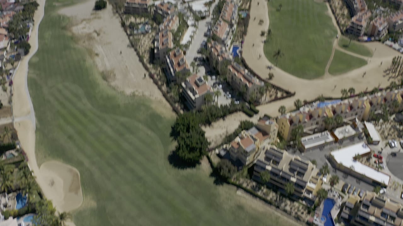 Aerial view of golf fairways, sand traps, buildings, and coastline.