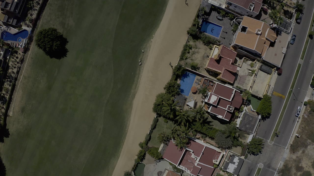 Overhead view of golf fairway beside residential homes and a road.