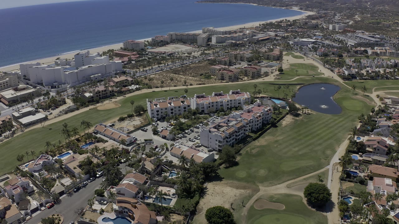 Drone view of coastal buildings, homes, golf greens, and pond