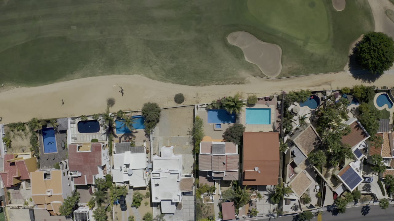 Overhead view of homes, pools, road, and golf course edge.