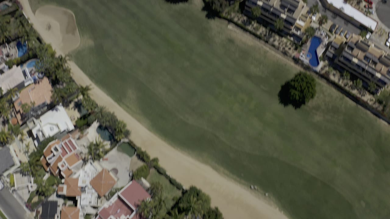 Aerial view of golf fairway, sand traps, homes, and palm-lined streets.