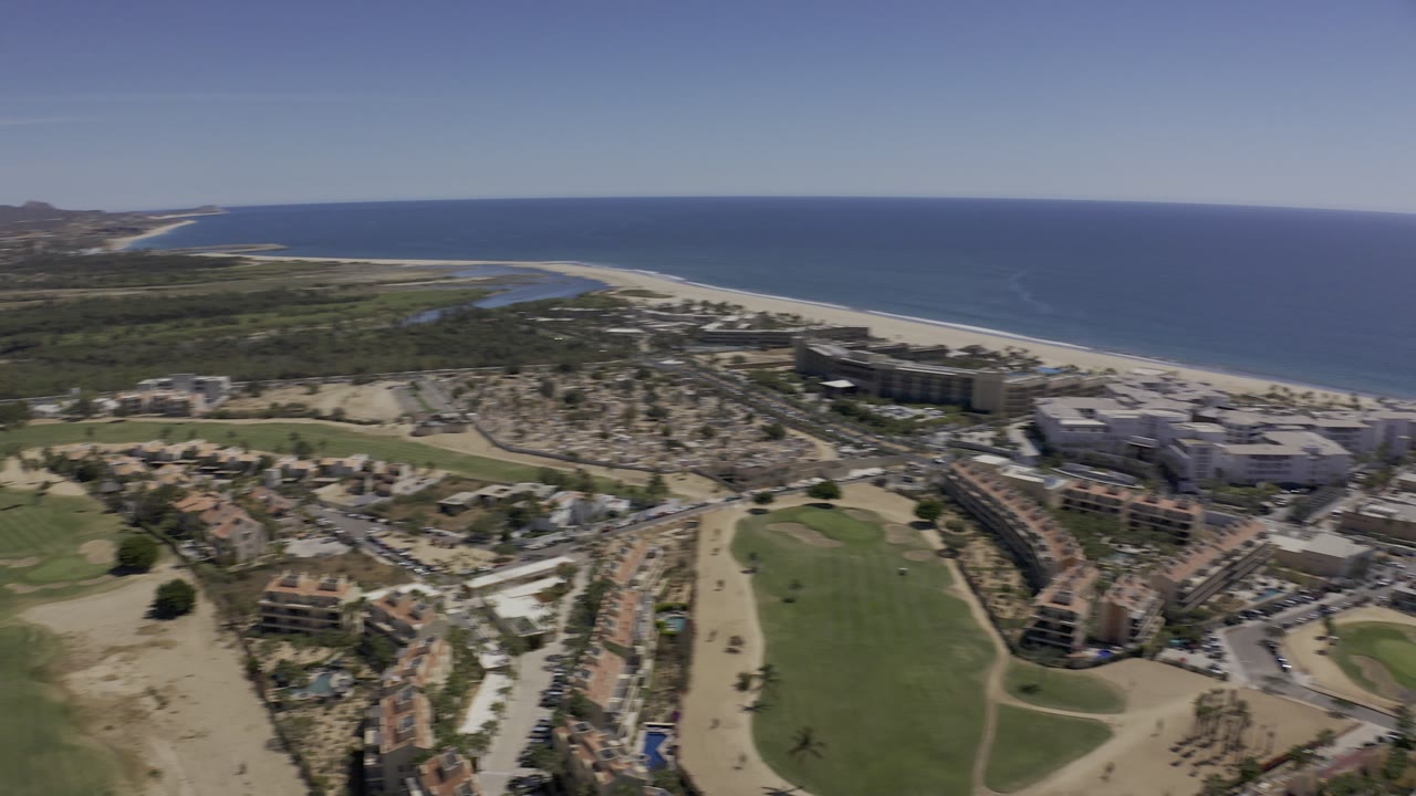 Aerial view of coastline, beach, ocean, green fairway, roads, and low buildings.