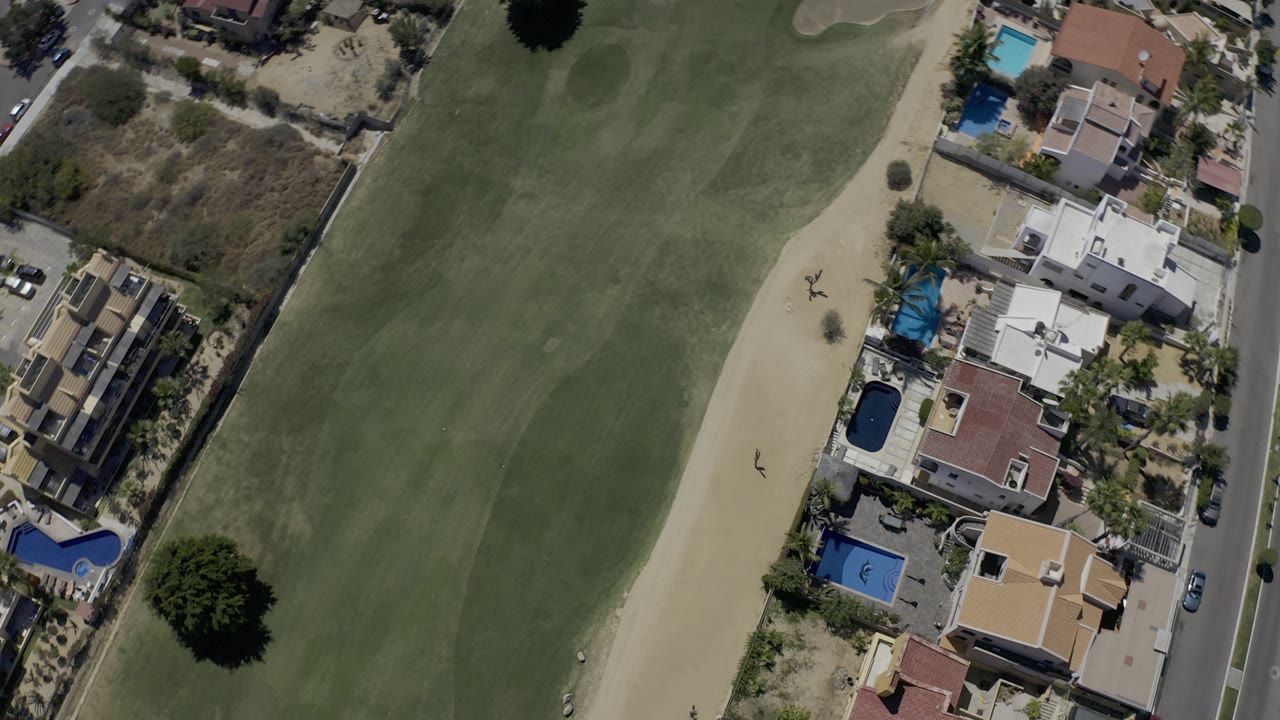 Overhead view of a golf fairway beside homes and pools.