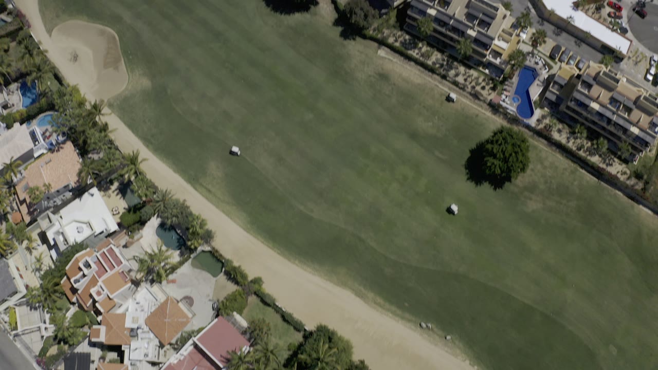 Top-down view of golf greens, sand bunker, homes, and resort buildings.