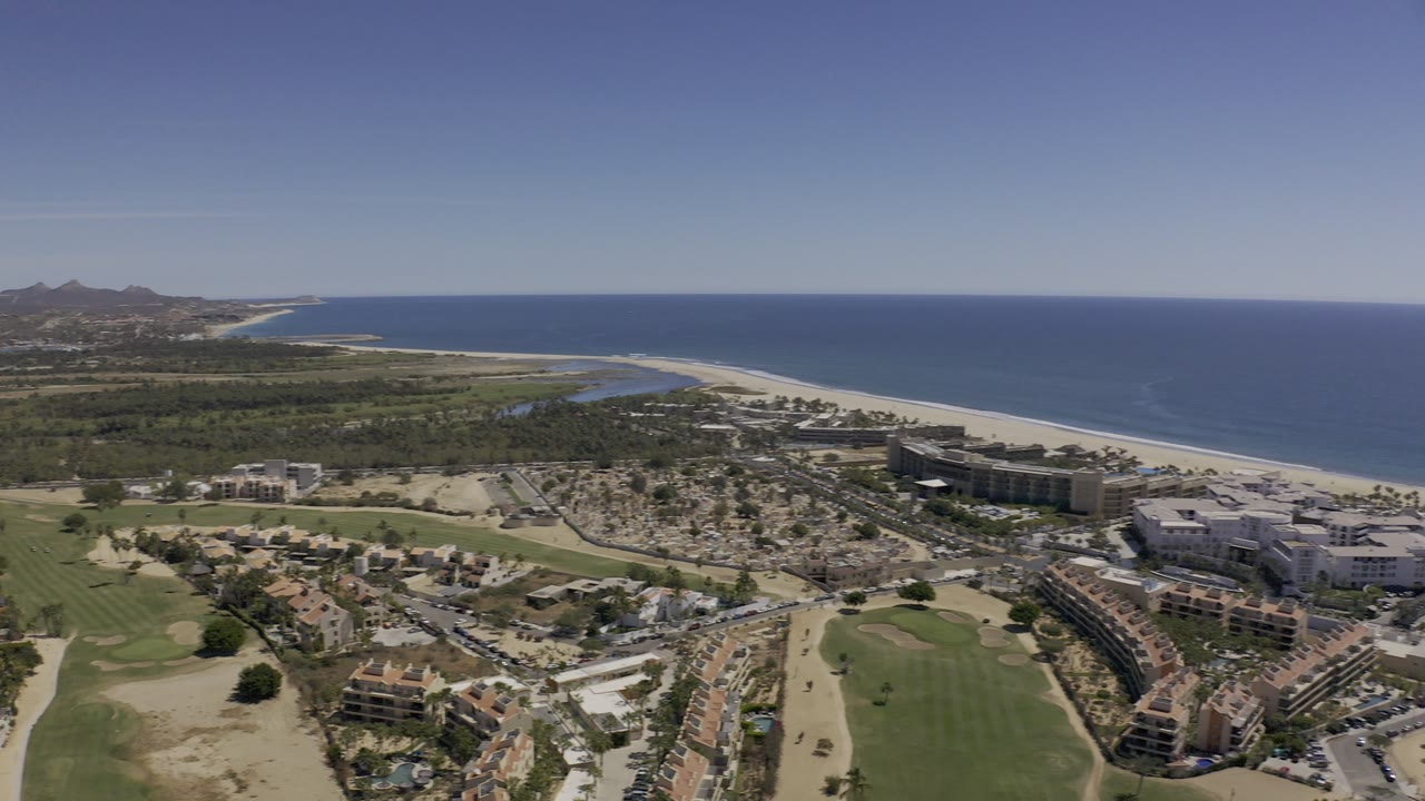 High view across Los Cabos shoreline, resort-area buildings, beach, and ocean.