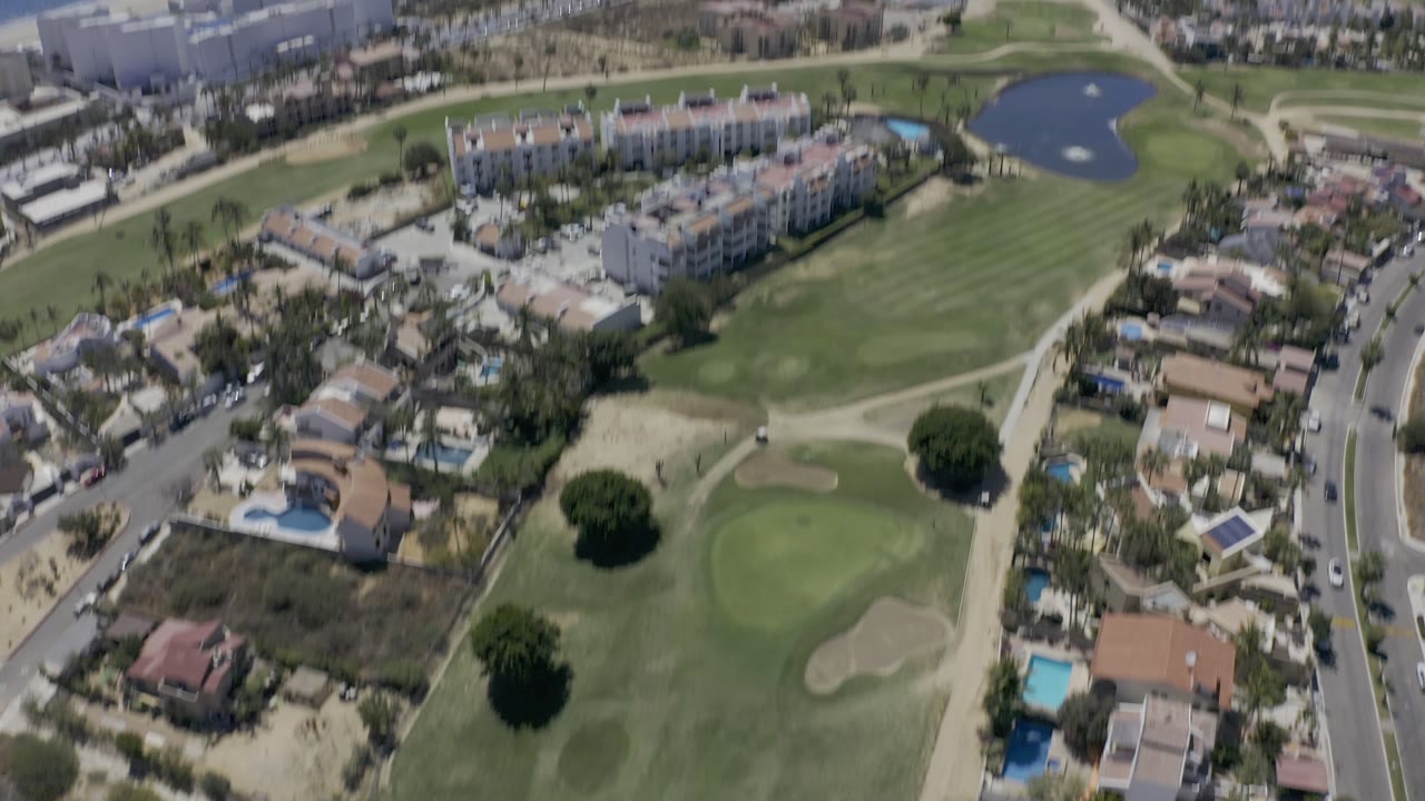 Aerial neighborhood view with golf green, pond, and beachfront buildings.