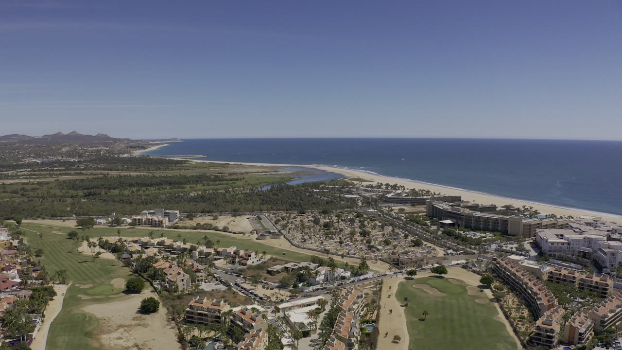 Aerial view of coastline, hotels, roads, golf course, and ocean.