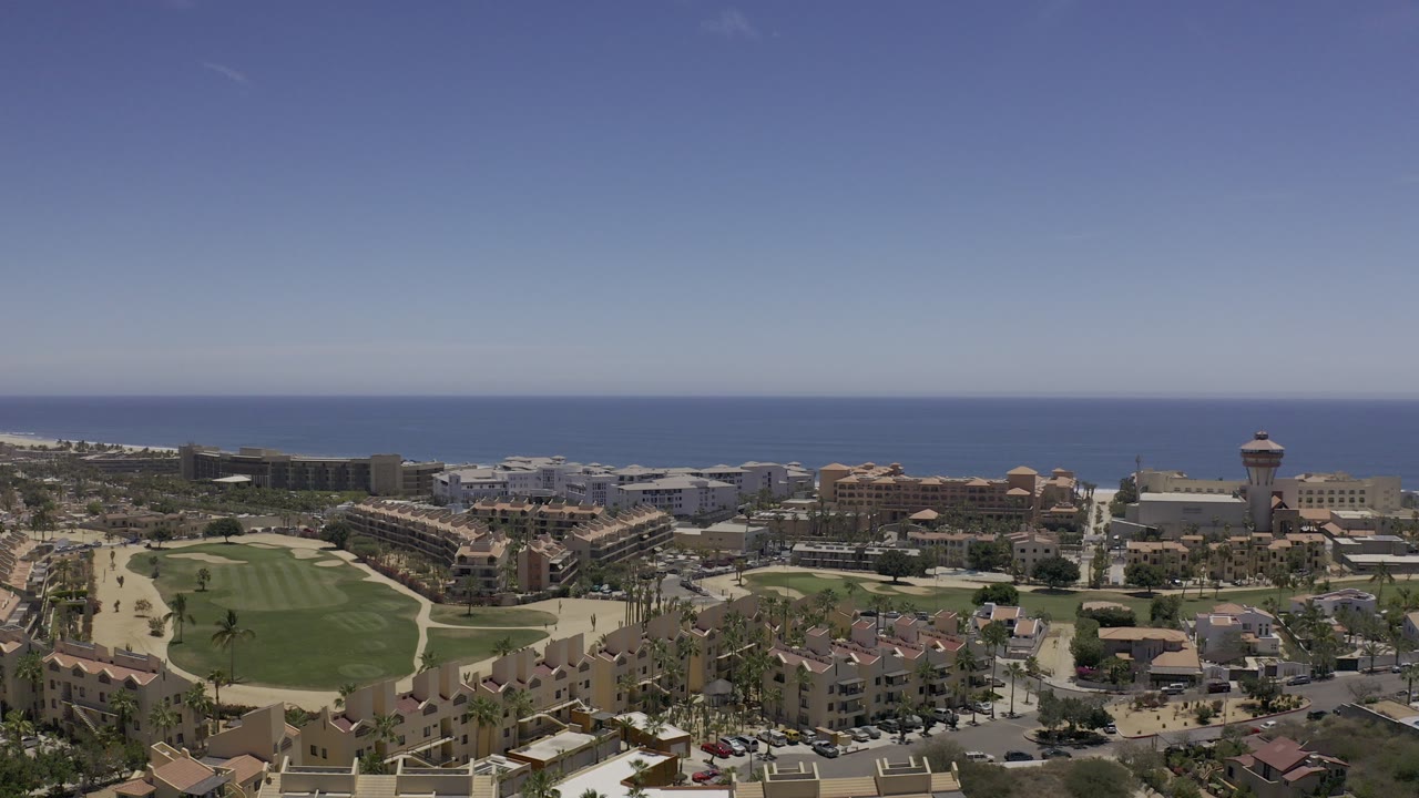 Aerial view of coastal buildings, golf green, and ocean horizon.