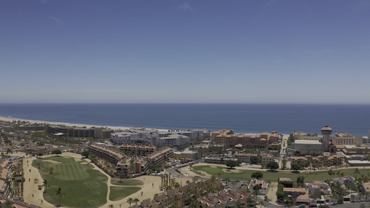 Aerial view of coastal buildings, golf greens, roads, and ocean horizon.