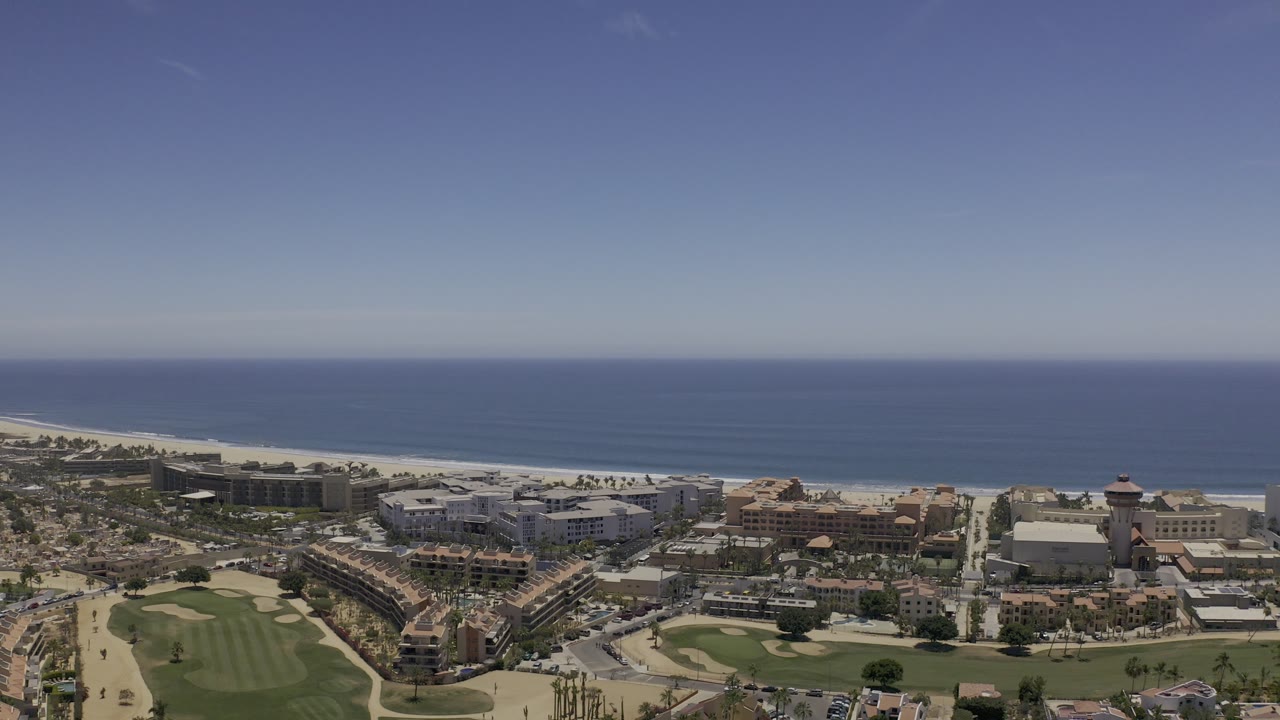 Wide aerial coastline with golf course, town buildings, beach, and sea