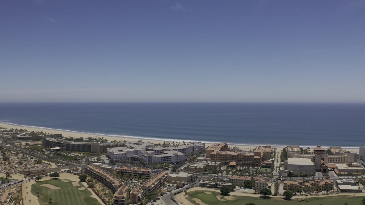Aerial coastline with resort-scale buildings, beach, sea, and clear sky.
