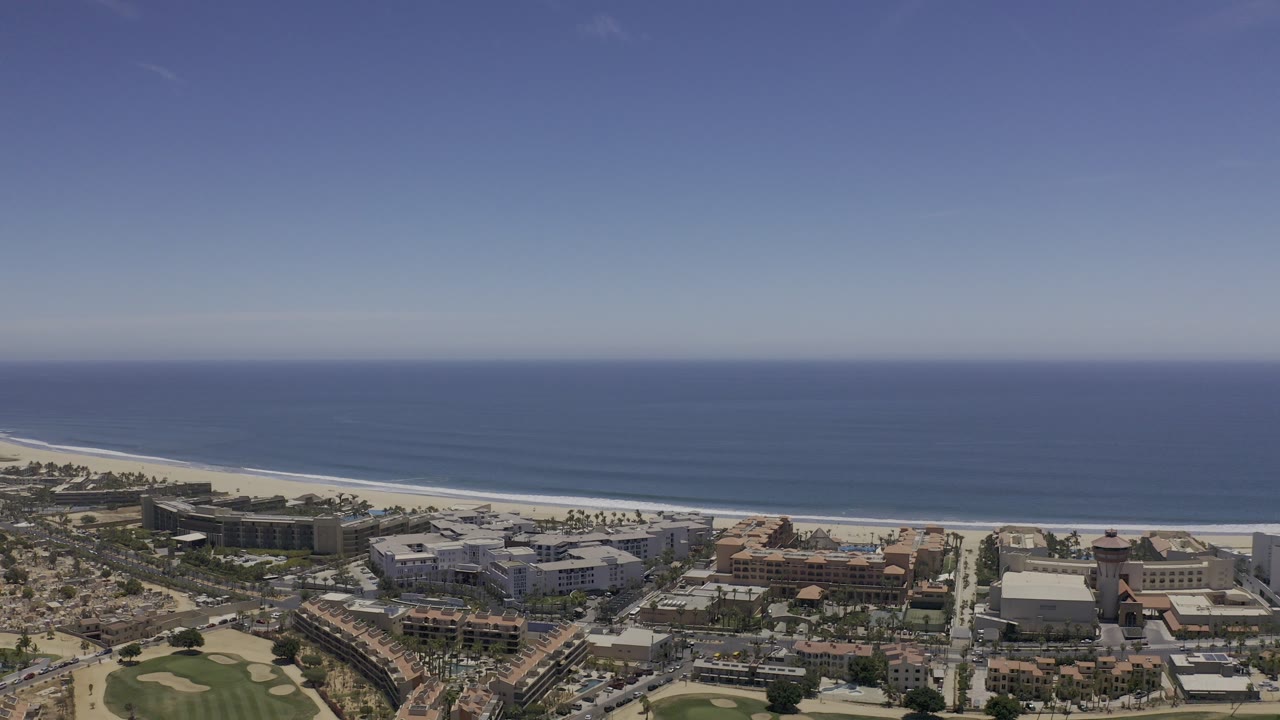 Wide aerial view of ocean, beach, buildings, and golf greens.