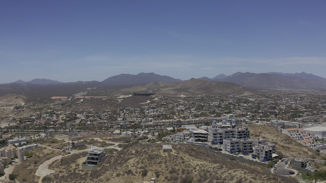 Wide aerial view of desert hills, buildings, roads, and distant mountains.
