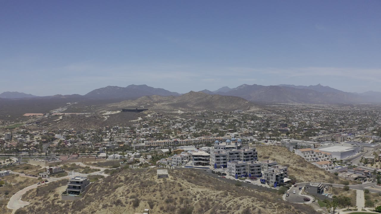 Aerial view over hillside roads, apartment buildings, residential blocks, and distant mountains.
