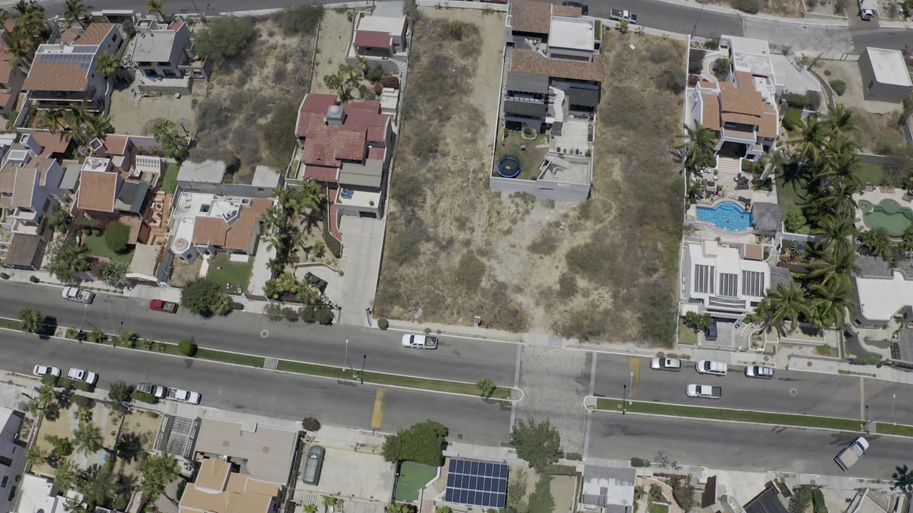 Overhead residential street with homes, dry lots, palms, cars, and pools