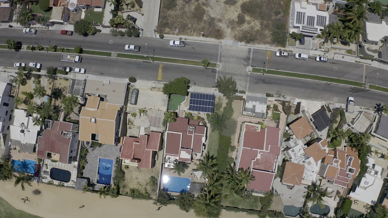 Top-down aerial view of beachside homes, road, pools, and sand.