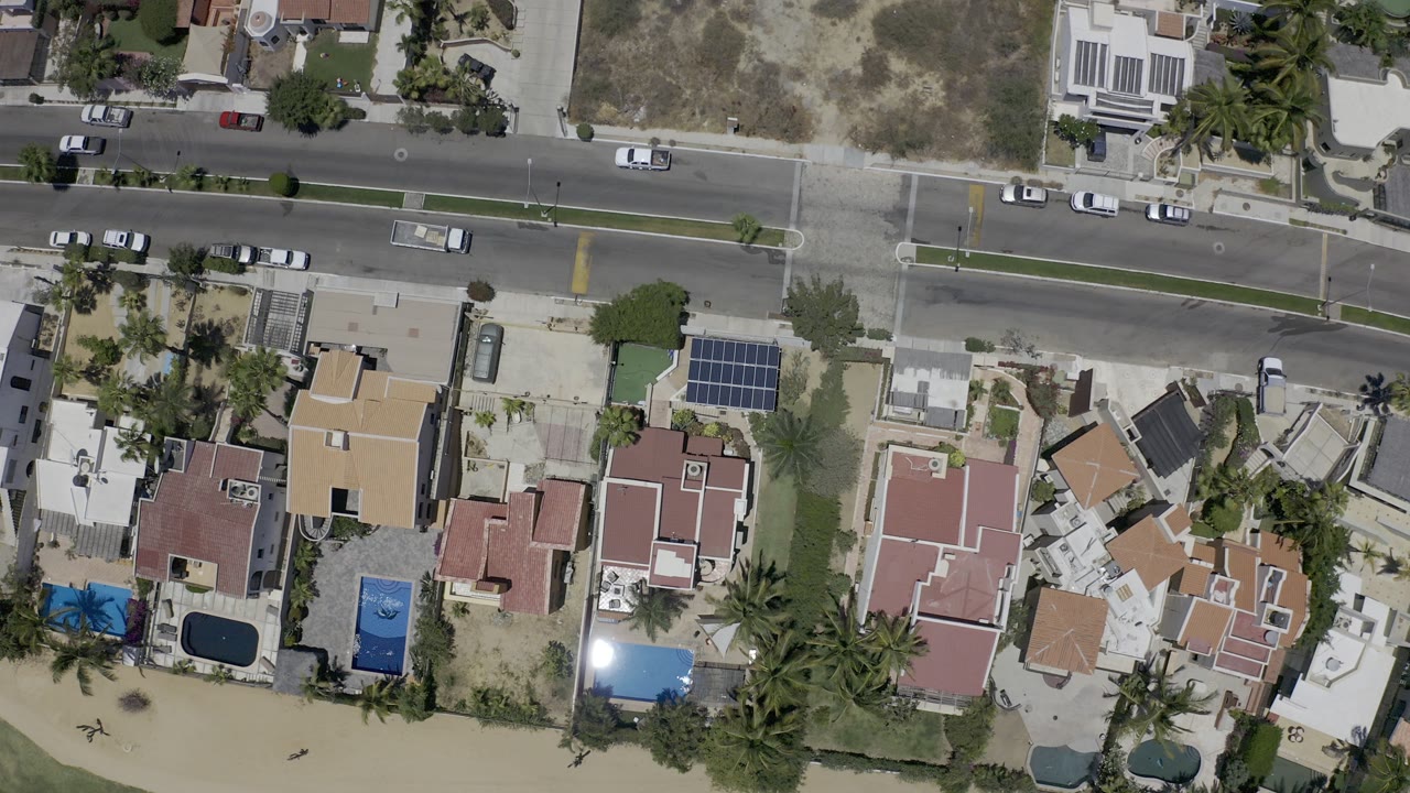 Overhead view of homes, yards, palms, and a road near sandy ground.