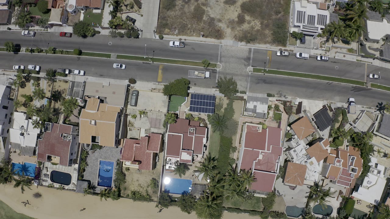 Overhead view of a two-lane road, cars, houses, palms, and beach sand.