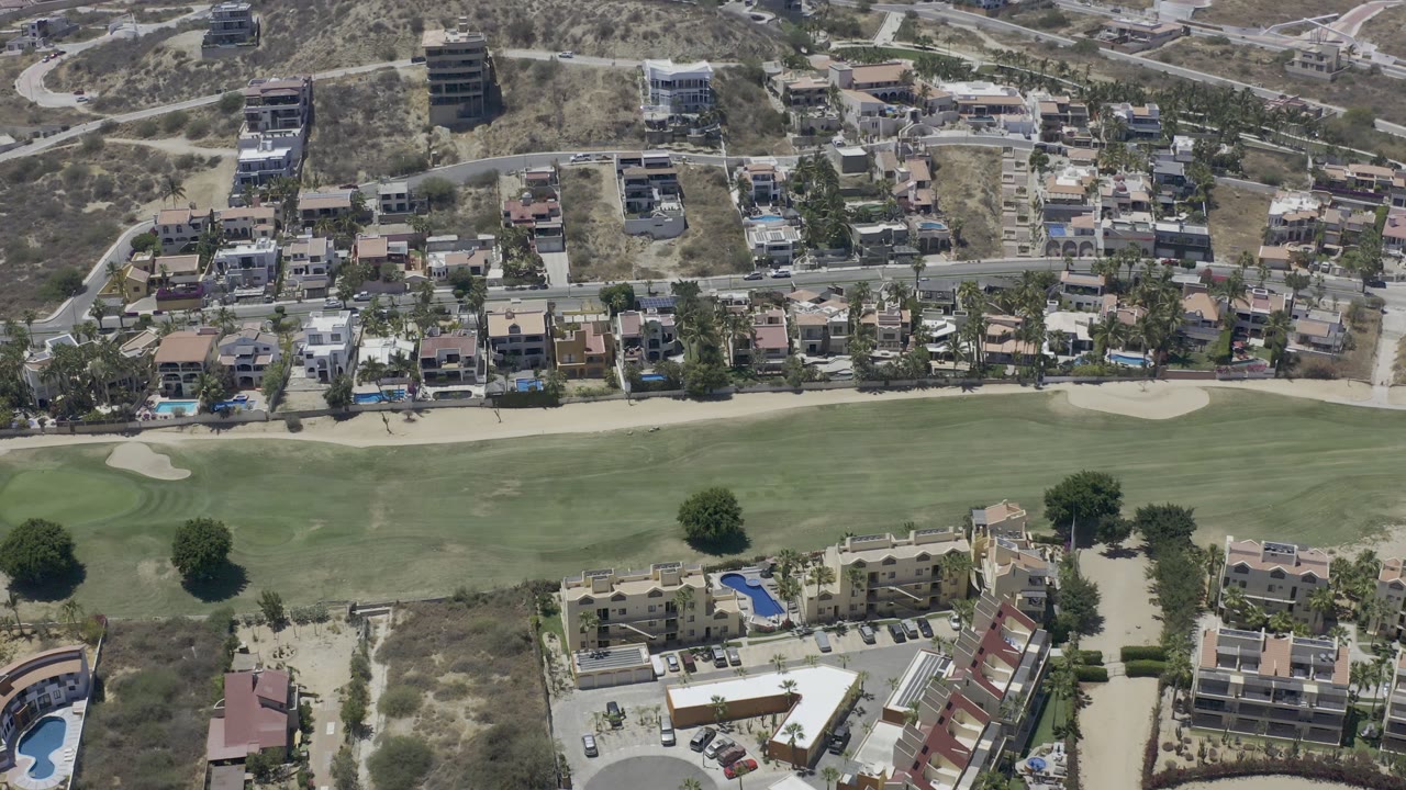 Aerial view of green grounds, homes, pools, trees, and dry hillside roads.