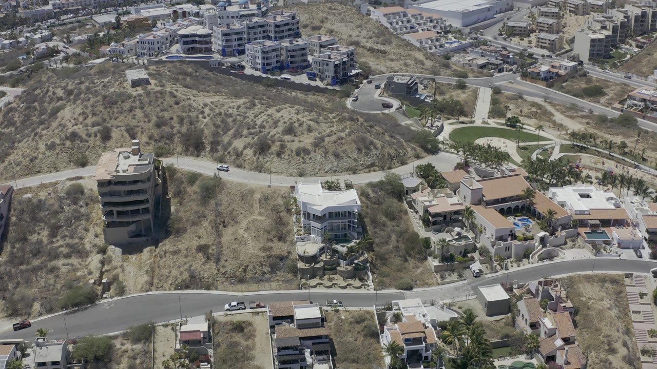 Elevated Los Cabos view with a large dry hill in the center, a curved road below, homes on both sides, and no visible people.
