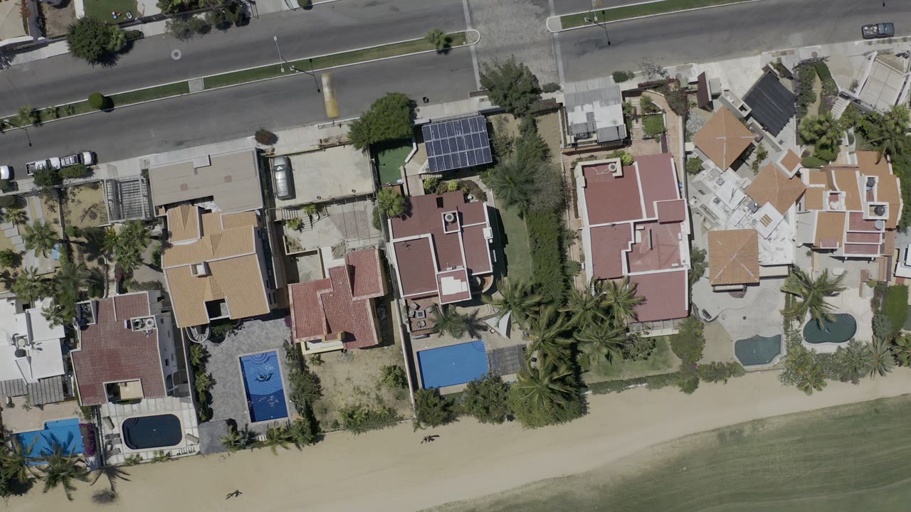 Top-down aerial view of beachfront homes beside a road and shoreline.