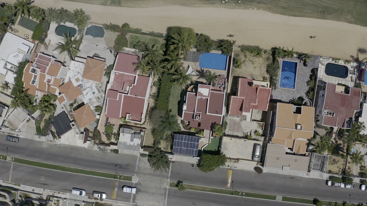 Overhead view of coastal homes, palm trees, sand, and a road.