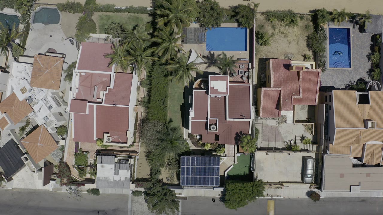 Overhead view of vacation rental roofs, pools, palms, and a residential street.