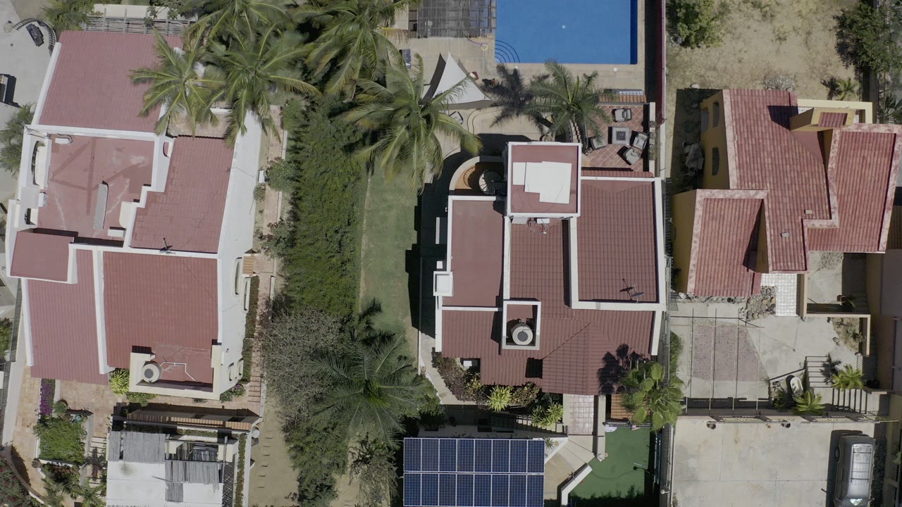 Overhead view of red-roofed homes, palms, garden hedges, and a blue pool corner.